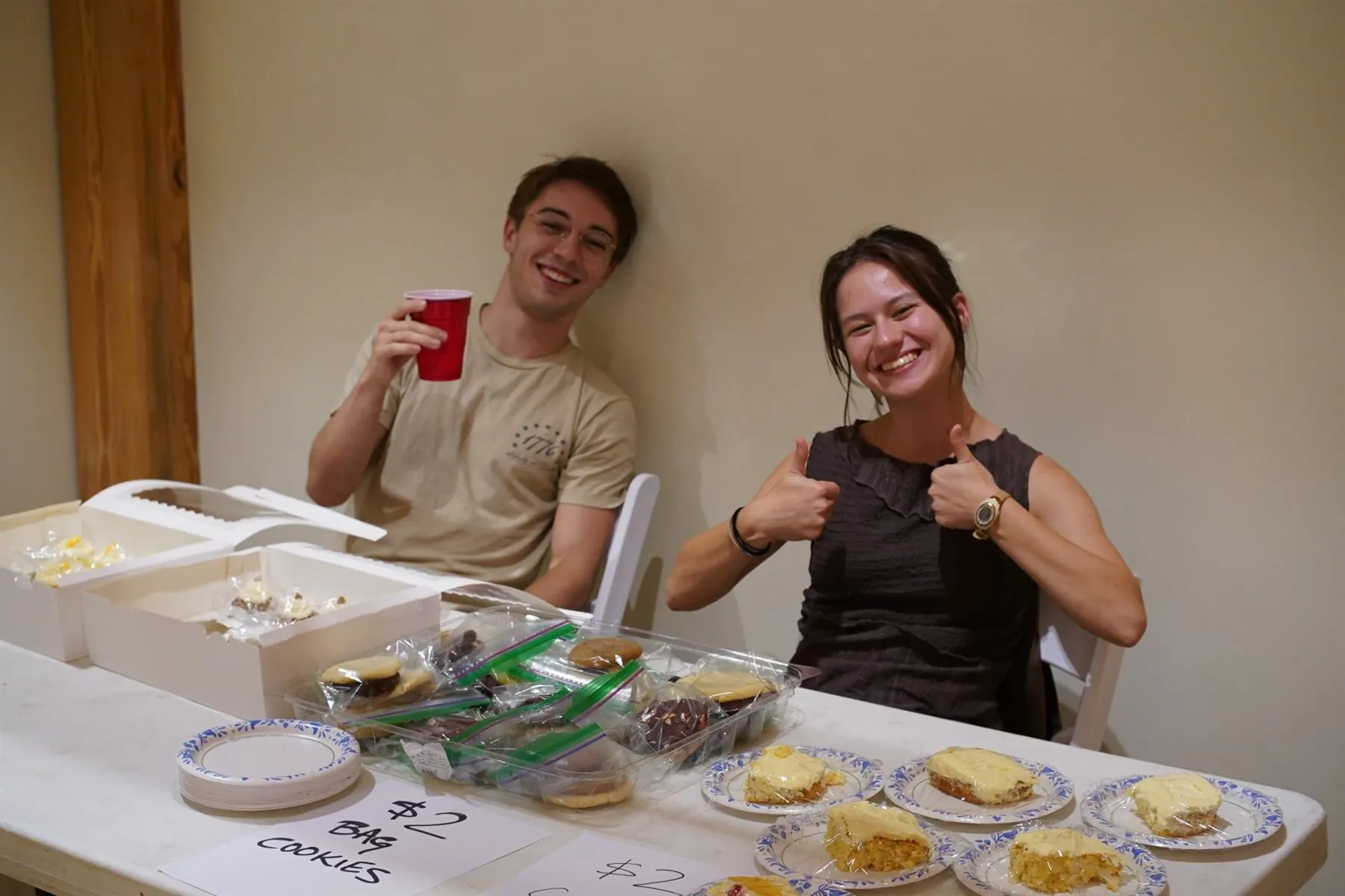 Two students giving a thumbs up behind a bake sale table